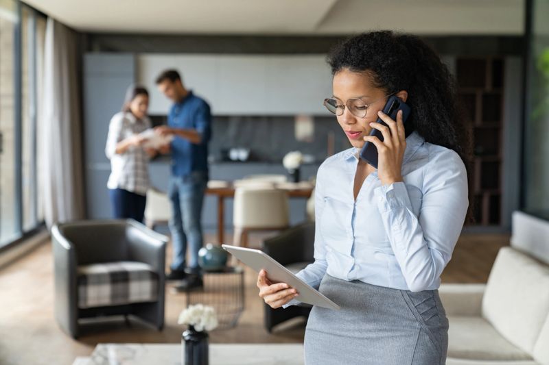 Latin American real estate agent talking on the phone and using a tablet while showing a house to a couple