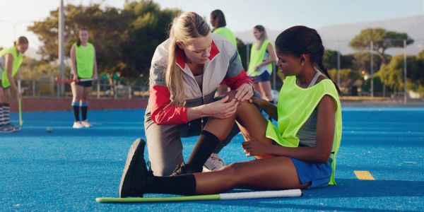 Coach examining injured hockey player's knee during practice.
