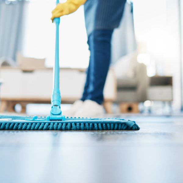 Person cleaning floor with a blue mop in a living room.
