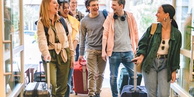 Group of young friends happily walking with luggage in an airport.
