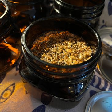 A jar filled with dried chamomile flowers on a patterned cloth.