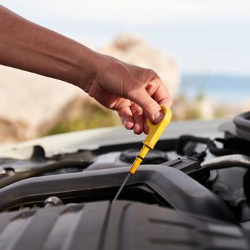 Hand pulling out a yellow oil dipstick from a car engine.