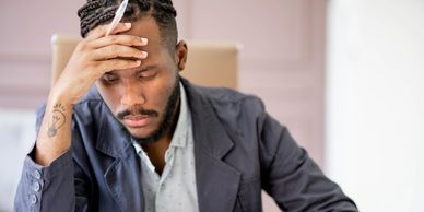 Man in blazer looking stressed and holding his forehead.