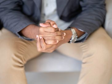 Cropped image of a male hands clasped and leaning forward. 