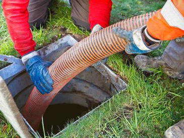 Person inserting a large orange hose into a ground hole.