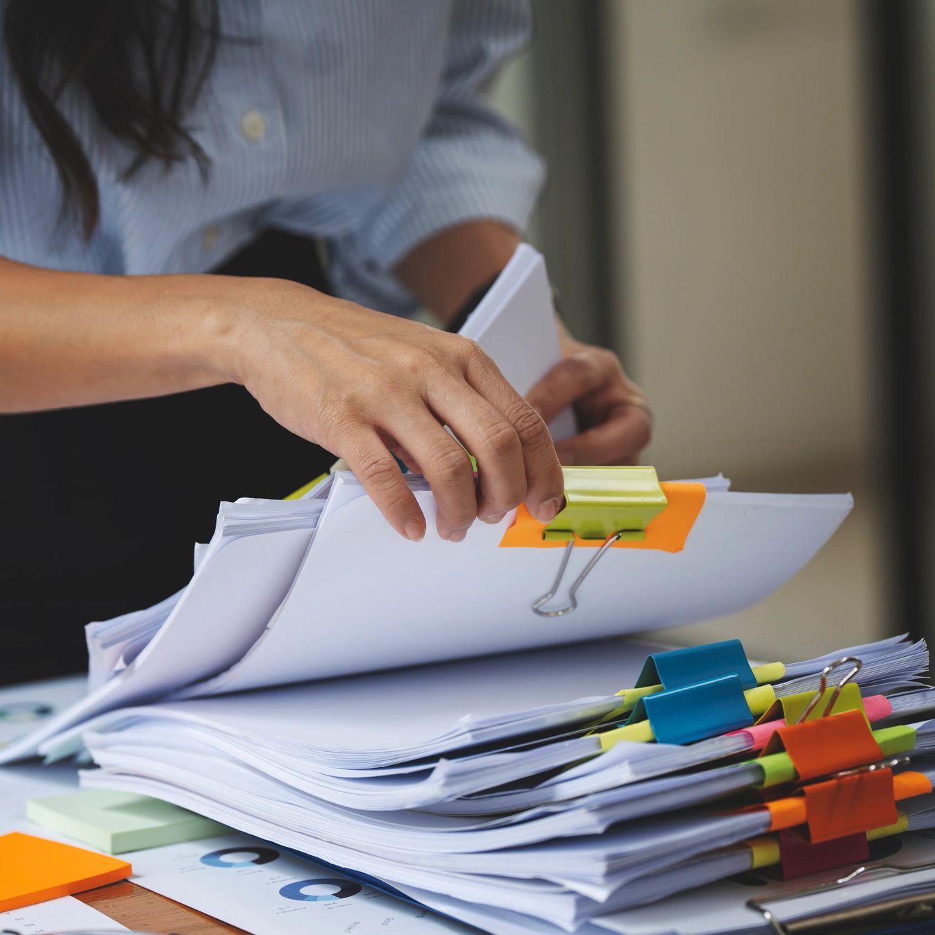 Person organizing large stacks of documents with colorful binder clips.