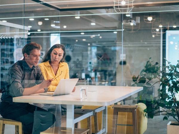 Two colleagues collaborating on a laptop in a modern office meeting room.