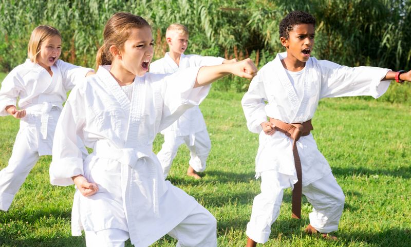 Positive children wearing white sports uniform practicing karate in park