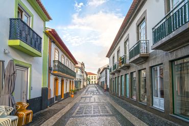 Charming cobblestone street with colorful buildings and balconies under a blue sky.