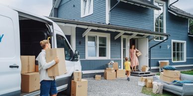 People moving boxes into a blue house from a white van.