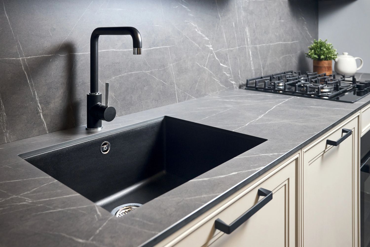 Modern kitchen countertop with black sink and faucet, and gas stove.