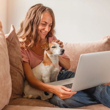 Woman smiling while using a laptop with her dog on the couch.