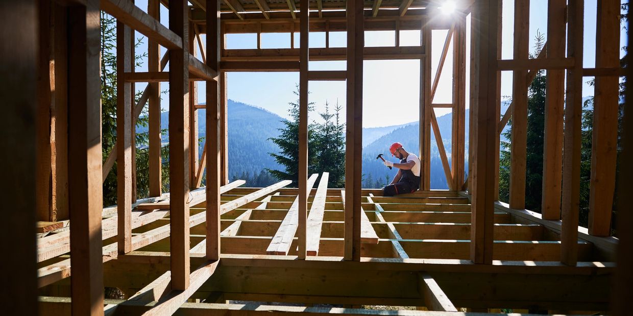 A construction worker building a wooden frame house in a mountainous area.