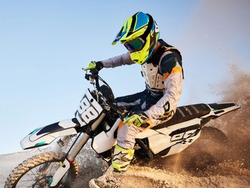 A motocross rider kicking up sand while turning sharply on a dirt bike.