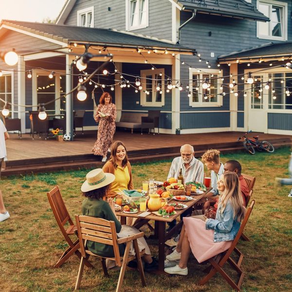 Family enjoying a festive outdoor dinner in the garden with string lights.