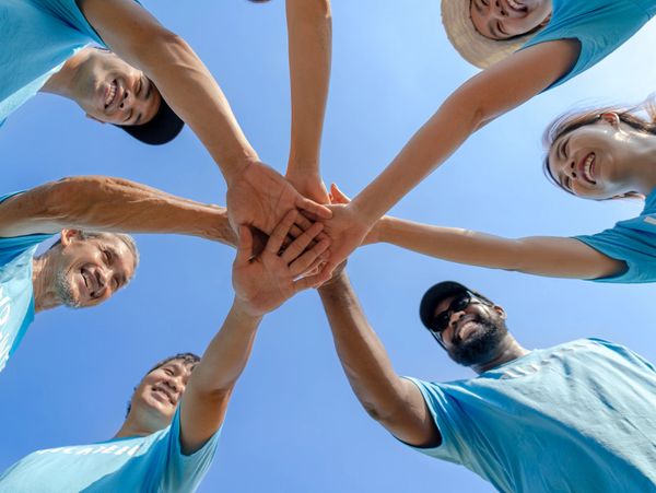 Group of people joining hands in a circle under a clear blue sky.
