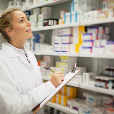 Pharmacist checking medication stock on shelves with clipboard.