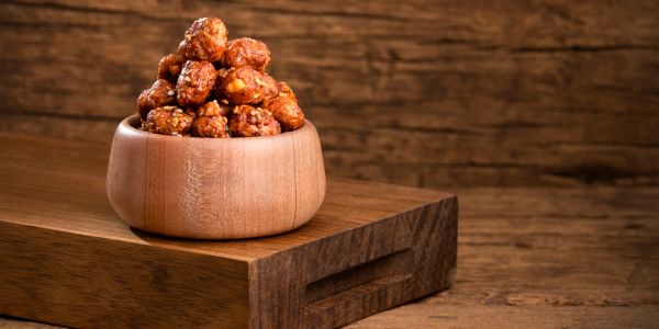 A wooden bowl filled with caramel-coated nuts on a wooden surface.