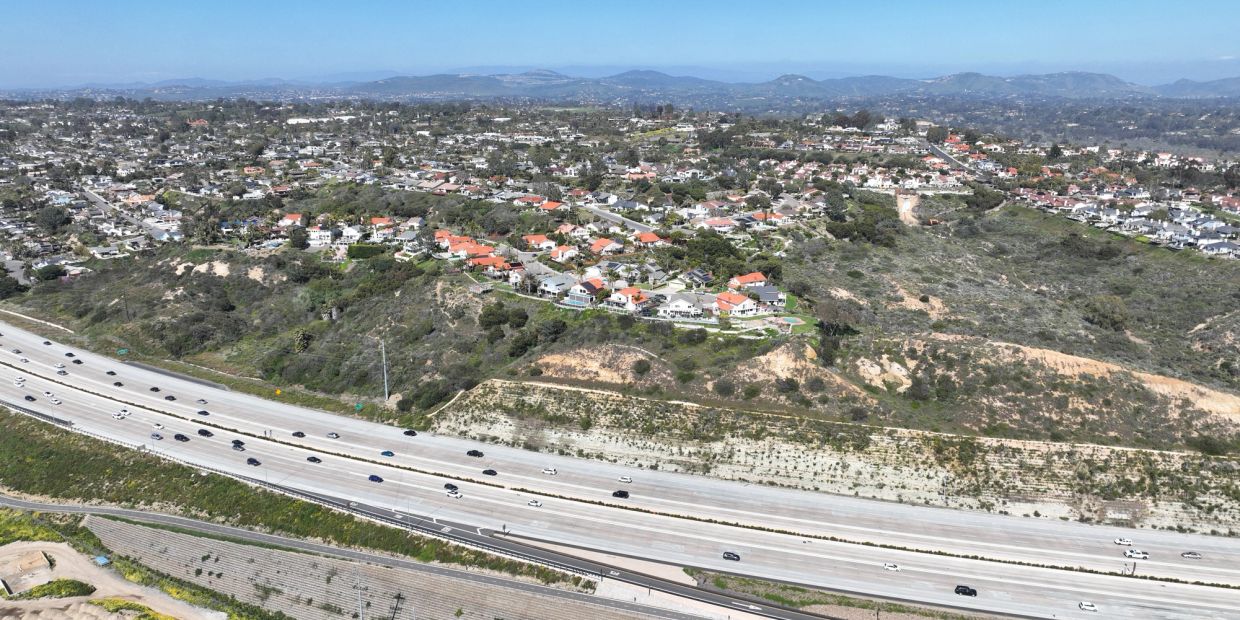 Aerial view of highway with suburban houses and hills.