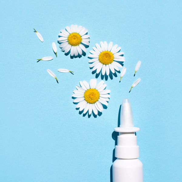 Nasal spray with daisy flowers and petals on a blue background.