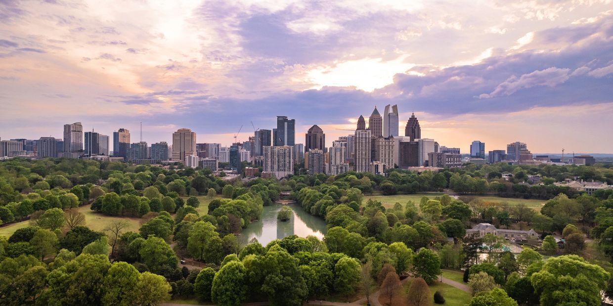 Urban skyline at sunset with abundant greenery and a river.