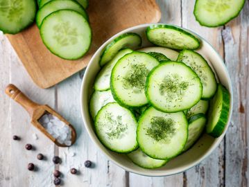 Fresh cucumber slices in a bowl with herbs sprinkled on top.
