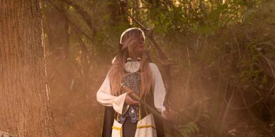 Woman in a mystical forest setting with a staff.