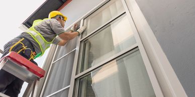 Worker in safety gear installing a window screen on a ladder.