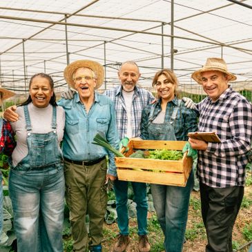 A diverse group of happy farmers in a greenhouse holding fresh vegetables.