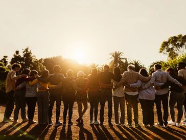 Group of people united with arms around each other at sunset.