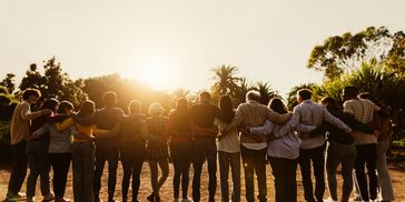 Group of diverse people with arms around each other at sunset.