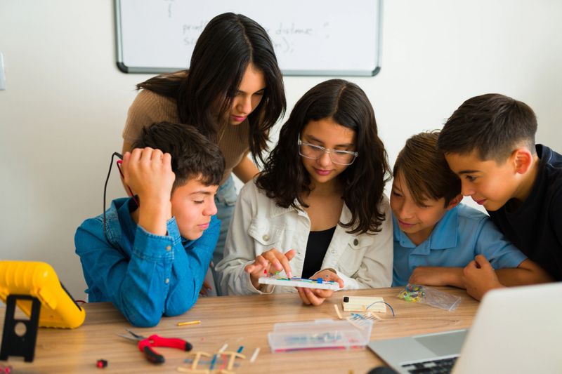 Group of teen students working and learning together on a robot prototype during their technology robotics class