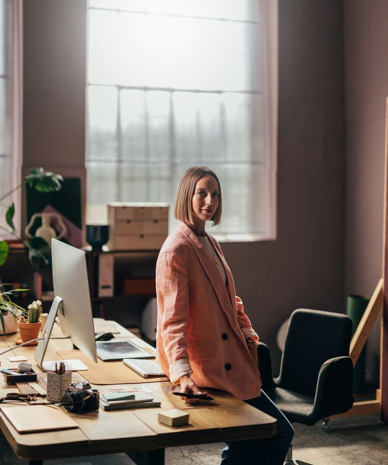 A portrait of a smiling confident Caucasian entrepreneur sitting on her office desk.