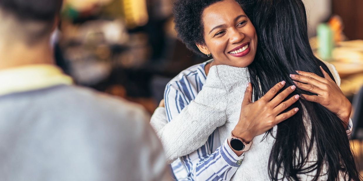 Two women warmly embrace, sharing a joyful moment together indoors.