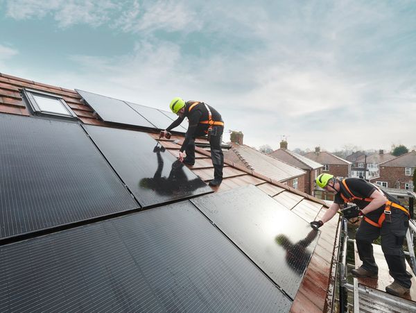 Technician installing solar panels on a dark roof.