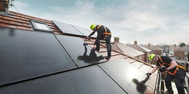 Two workers install solar panels on a rooftop under a clear sky.