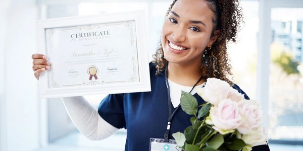 Happy medical intern holding certificate and flowers.