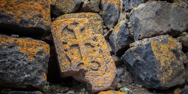 Ancient stone with a carved cross, covered in orange lichen.