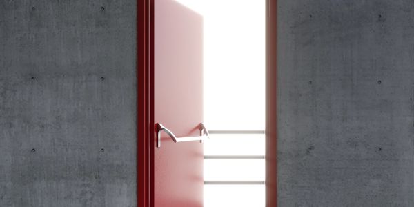 Red door slightly open in concrete wall with bright light beyond.