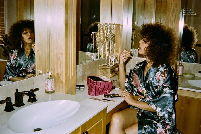 Woman in floral robe applying lip gloss in a bathroom mirror.
