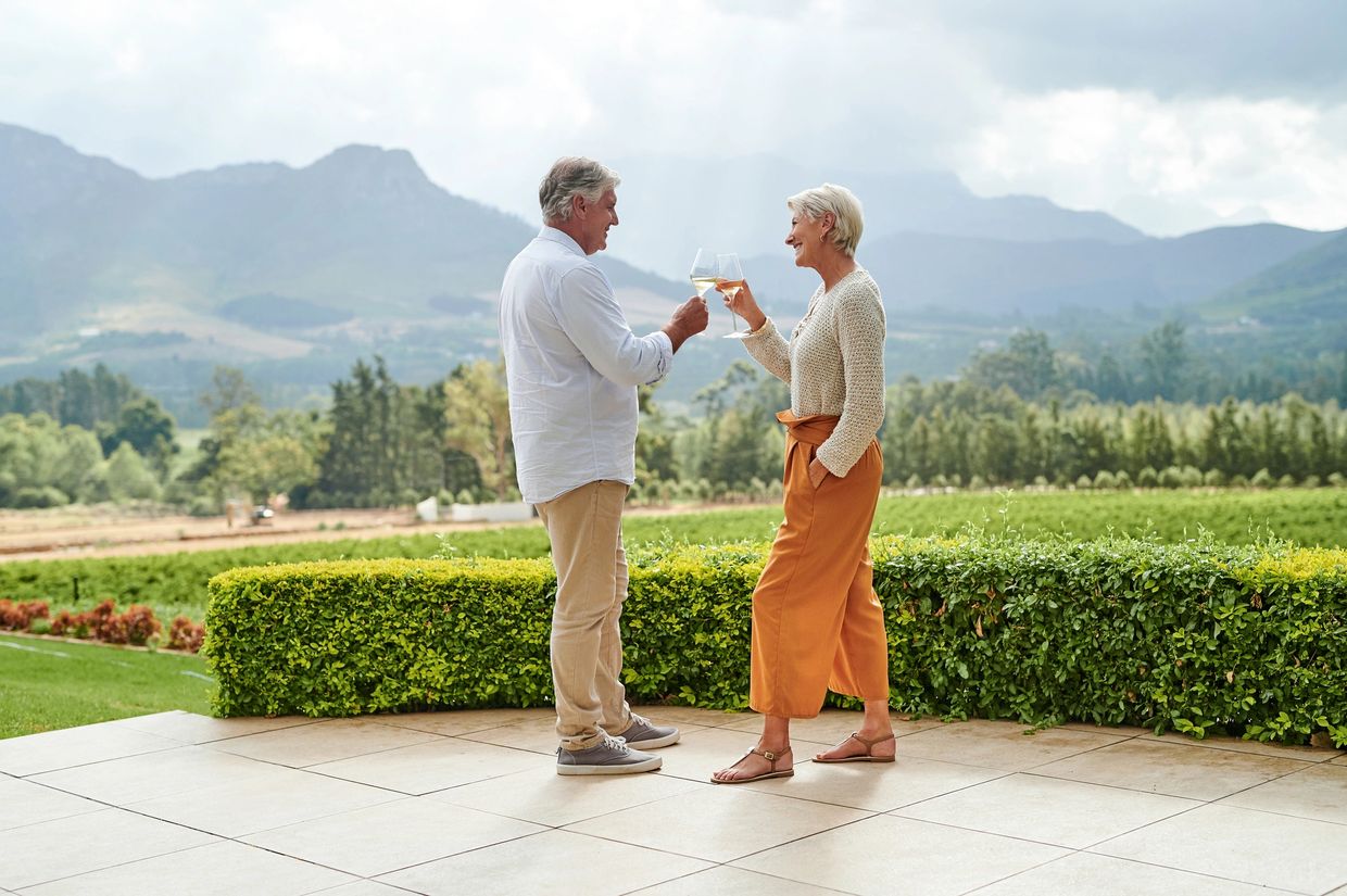 Older couple toasting with wine outdoors against a mountain backdrop.