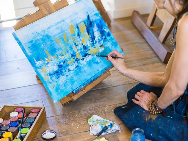 Artist painting an abstract blue and yellow cityscape on canvas.
