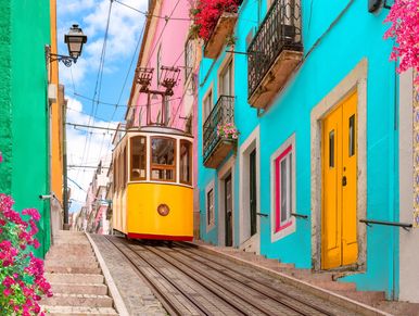 Colorful tram ascending a steep street lined with vibrant buildings and flowers.