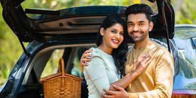 Couple smiling and hugging near an open car trunk with a picnic basket.