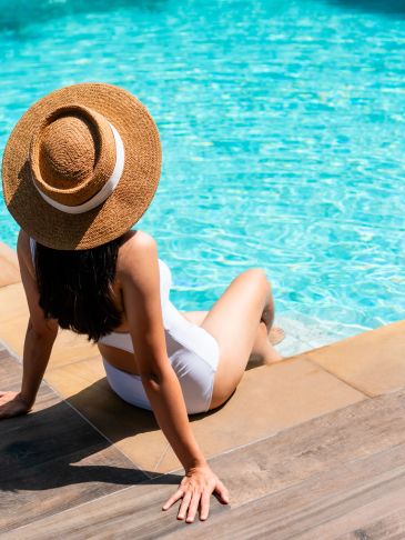 Woman in white swimsuit and straw hat by the pool.