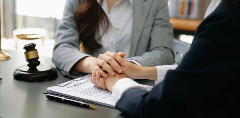 Business people compassionately holding hands and discussing contract papers with laptop and tablet at office room.