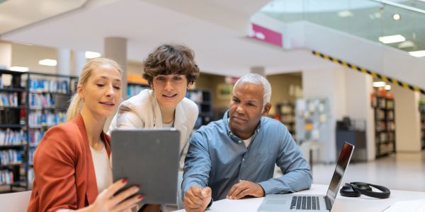 Three people looking at a tablet in a library.
