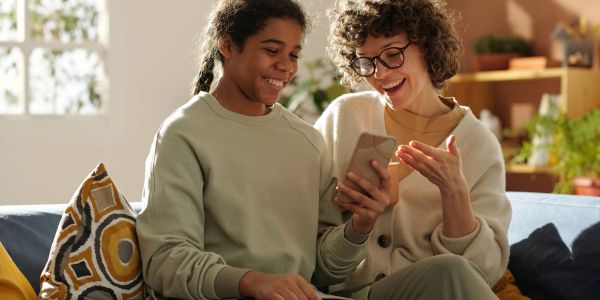 Two women smiling while using a smartphone.