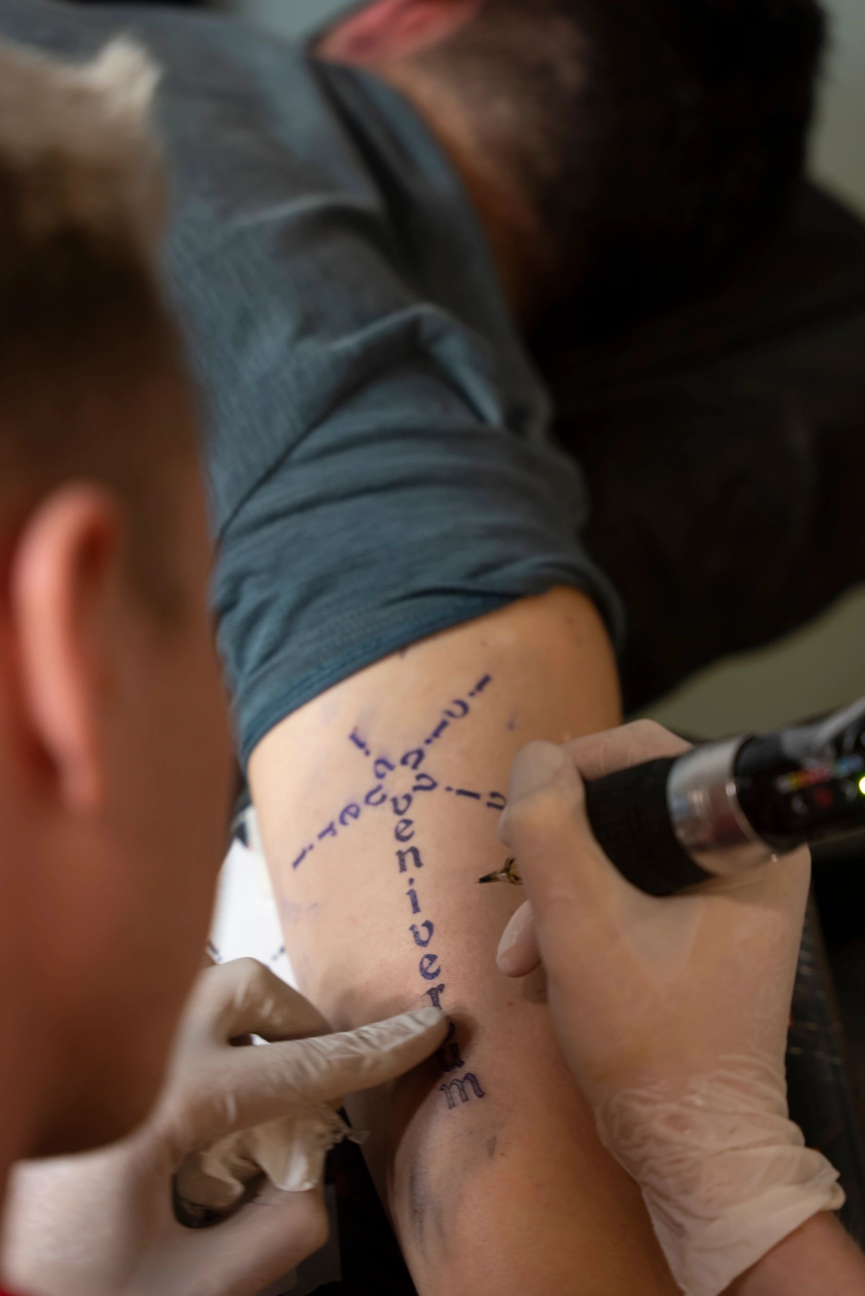 young tattoo artist doing tattoos to young man arm’s
