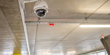 Security camera mounted on a concrete ceiling in a parking garage.